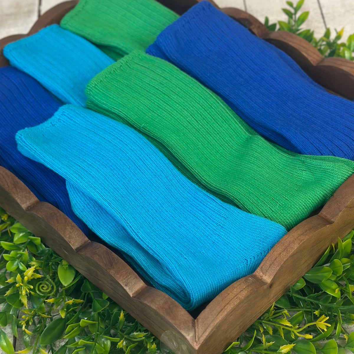 Folded blue and green socks in a wooden basket with a natural background