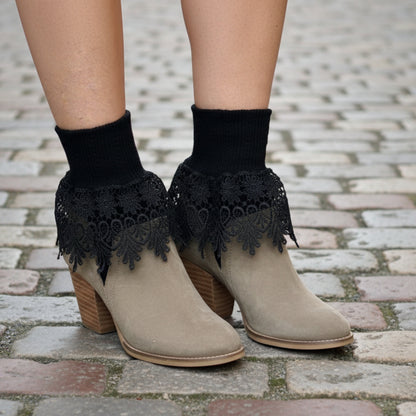 Beige ankle boots with black lace details worn on a cobblestone street with autumn leaves.