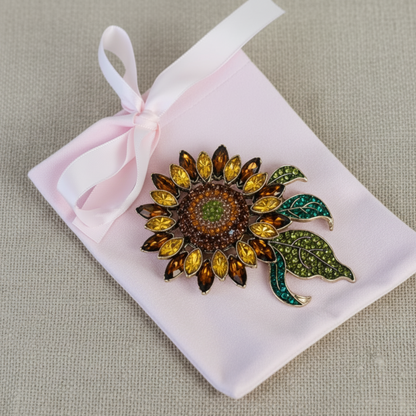 Sunflower-shaped brooch with gemstones on a pink satin bag against a beige background, Sunflower Crystal Brooch Pin 3x4" | Amber & Teal Rhinestone Brooch