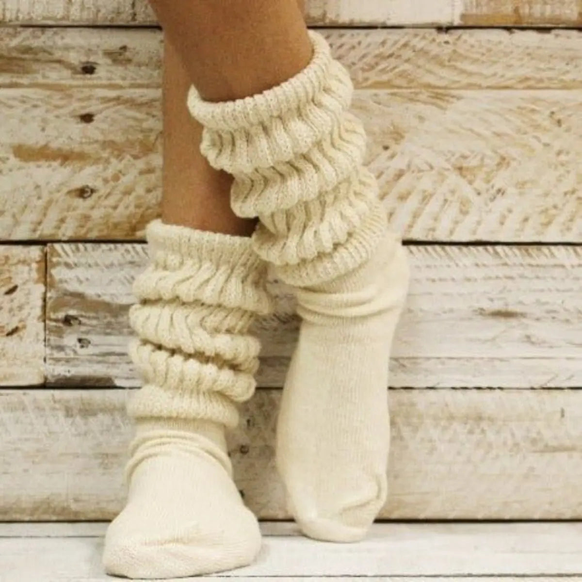 beige knitted leg warmers worn over white socks against a wooden background