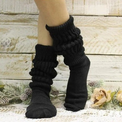 Black ribbed leg warmers worn by a person on a decorative background with flowers and pine cones.