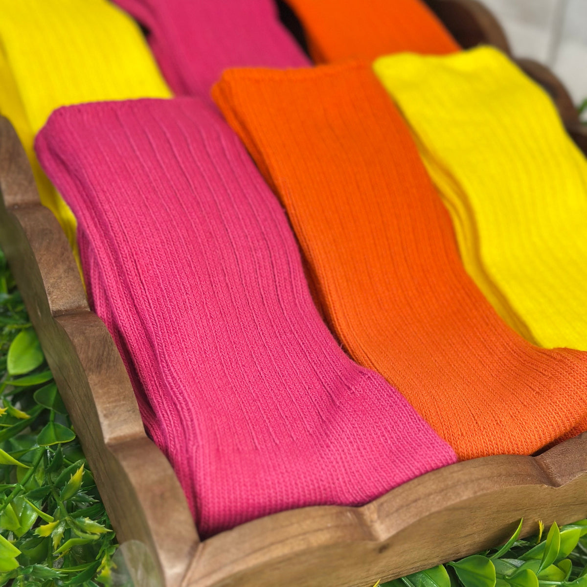 Colorful socks on a wooden surface with greenery in the background by Catherine Cole